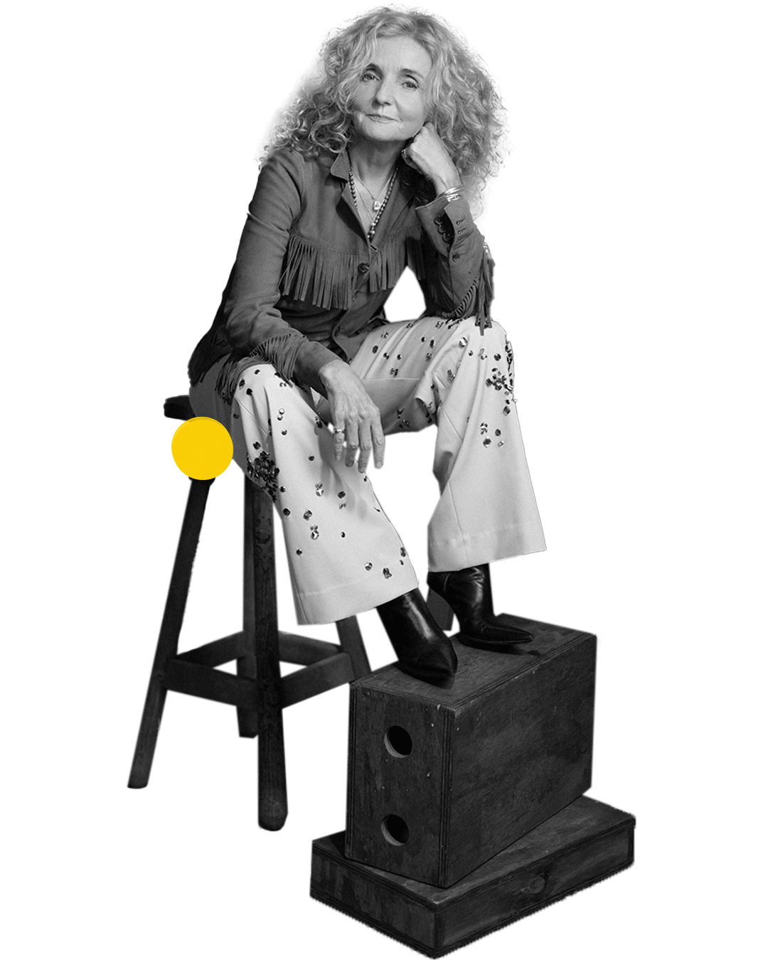 Patty Griffin seated on a stool with one leg resting on stacked wooden boxes.